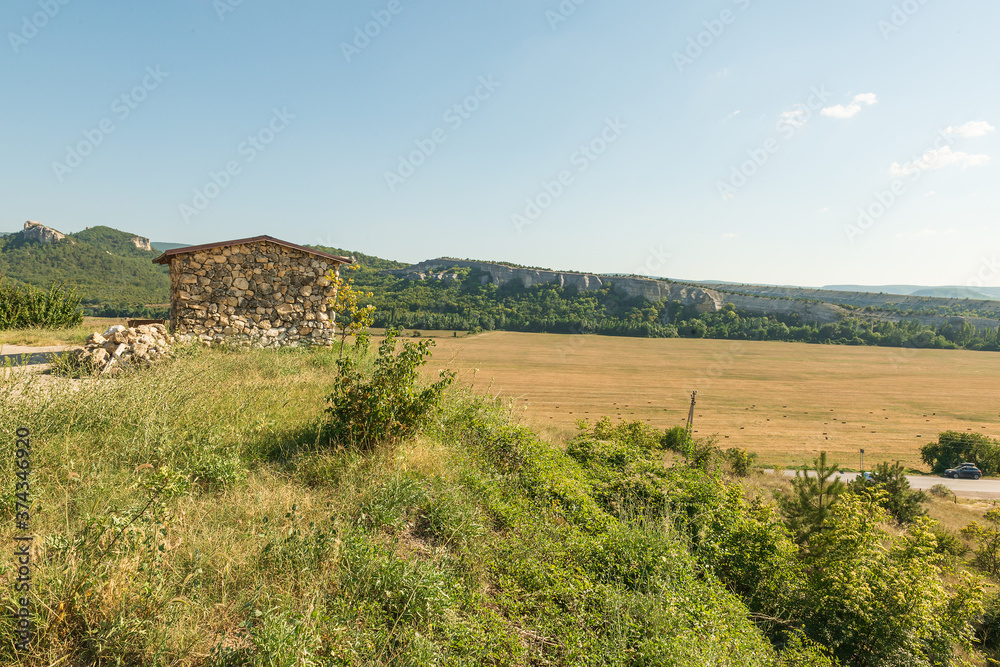 Crimea, landscape, a hill on which a stone building, a view from the hill on a mown field and stacked bales of hay or straw on it