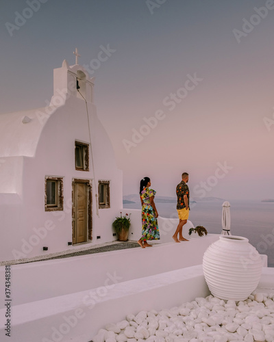 Santorini Greece, young couple on luxury vacation at the Island of Santorini watching sunrise by the blue dome church and whitewashed village of Oia Santorini Greece during sunrise during summer photo