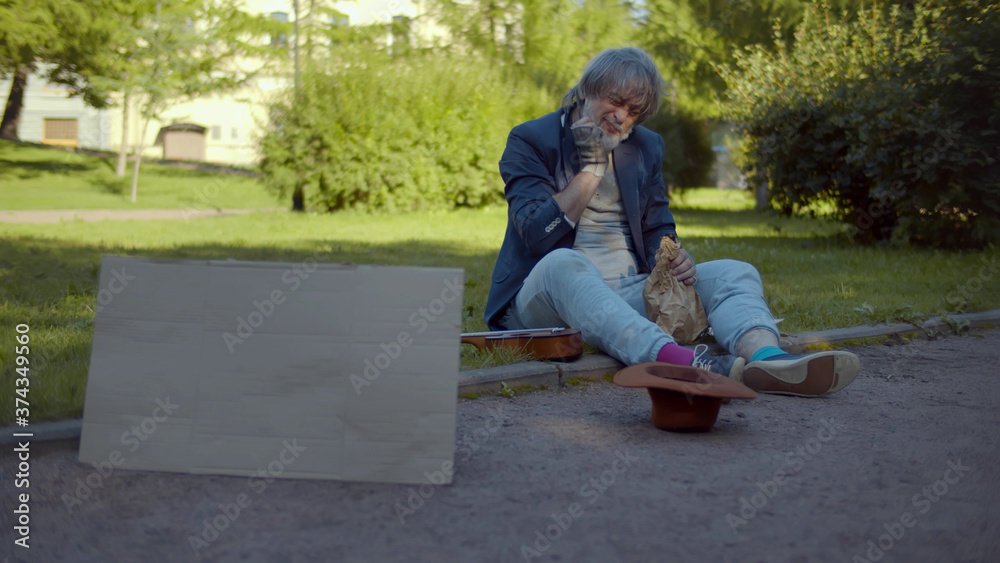 Senior homeless man sitting on ground scratching bears with blank cardboard sign Senior homeless man sitting on ground scratching bears with blank cardboard sign