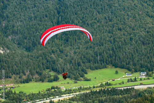 Parapendio, con paracadute rosso e tuta rossa su uno sfondo di abeti di montagna, perfetto per riviste, magazine, copertine e pubblicità photo