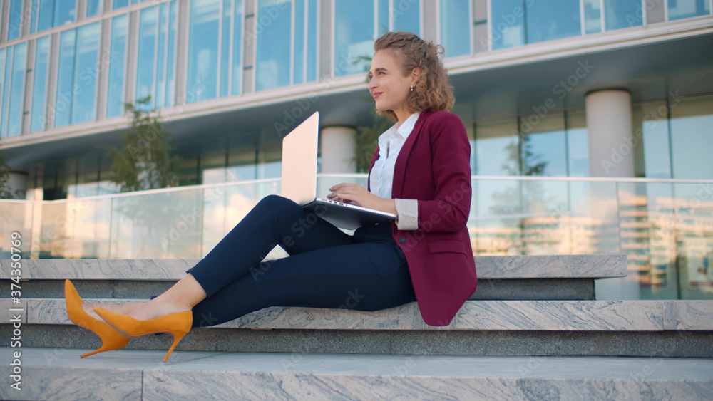 Beautiful businesswoman with laptop sitting on stairs outdoors