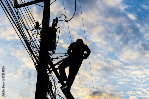 Silhouetted electricians working at electric pole in blue sky background. photo