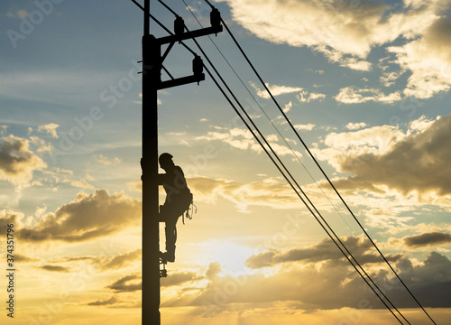 Silhouette man works with electricity on a pole with the sunset in the sky.