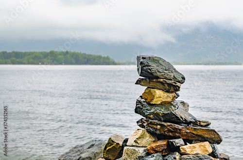 various stones stacked on top of each other in the form of a pyramid lie on the shore of the lake in foggy rainy weather photo