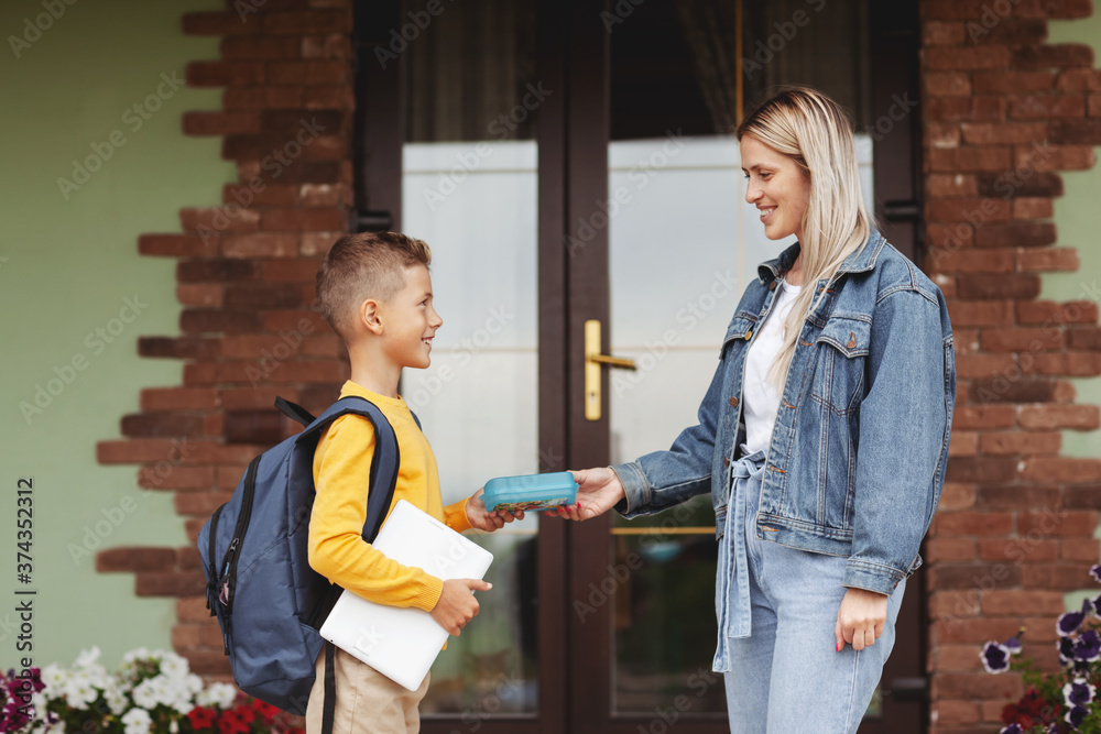 Fototapeta premium Mom escorts her son to school, serving him lunch in a box. Back to school