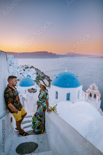 Santorini Greece, young couple on luxury vacation at the Island of Santorini watching sunrise by the blue dome church and whitewashed village of Oia Santorini Greece during sunrise during summer photo