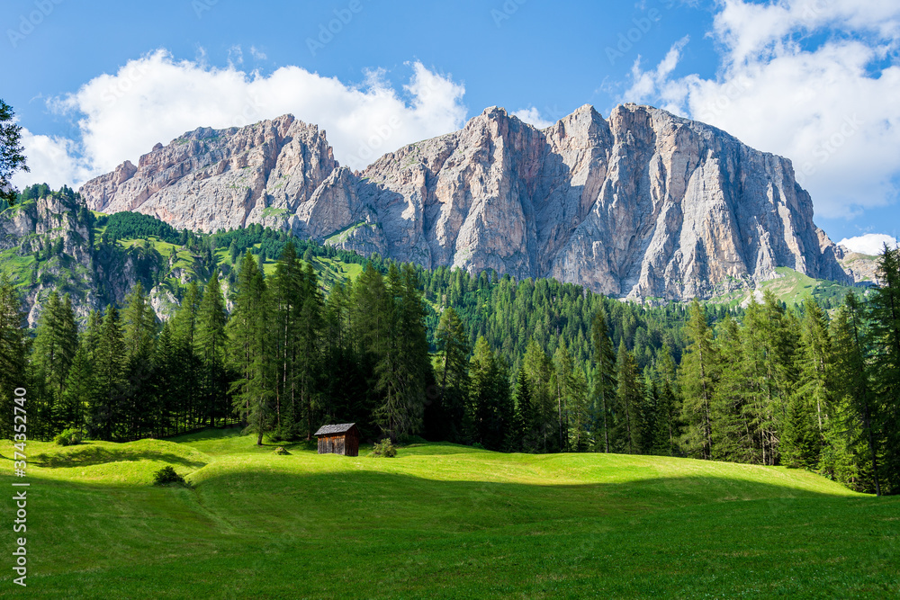 Isolated mountain hut surrounded by green meadows during summer. High Dolomite peaks of Italian Alps are visible in the background. Val Badia - South Tyrol, Italy