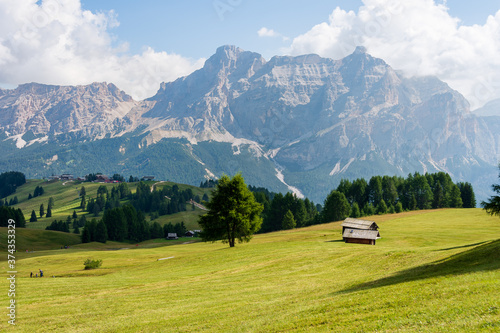 Isolated mountain huts surrounded by green meadows during summer. High Dolomite peaks of Italian Alps are visible in the background. Val Badia - South Tyrol, Italy