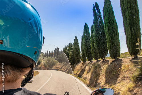 Fototapeta Naklejka Na Ścianę i Meble -  A guy drives a scooter in the streets among the cypresses of the Tuscan hills