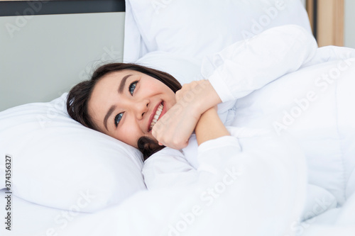 Beautiful young woman sleeping in a white bed. Pretty young girl on bed in modern apartment in the morning. Beautiful Asian girl with attractive smile enjoy fresh soft bedding linen mattress in white.