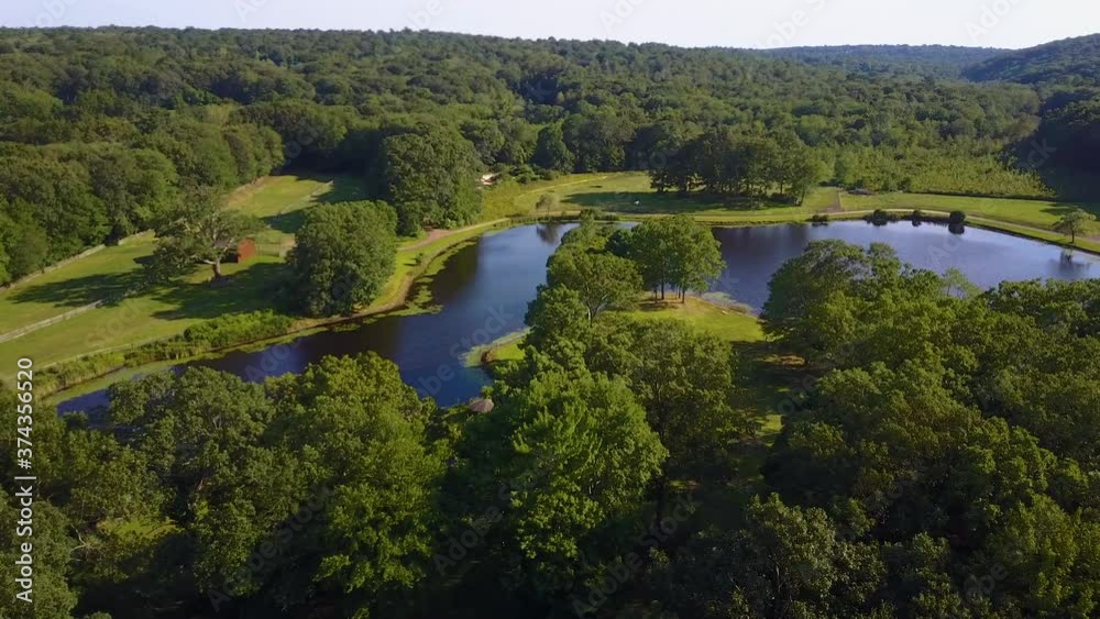 Overpassing aerial drone shot of horse farm and pond surrounded by green foliage Overpassing aerial drone shot of horse farm and pond surrounded by green foliage