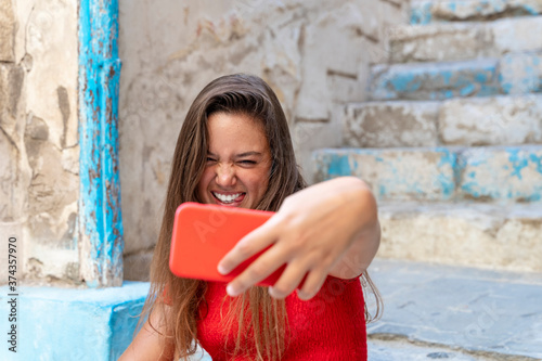 Attractive young girl smiling and taking a selfie in the street on a sunny day dressed in casual red clothes © Supermelon