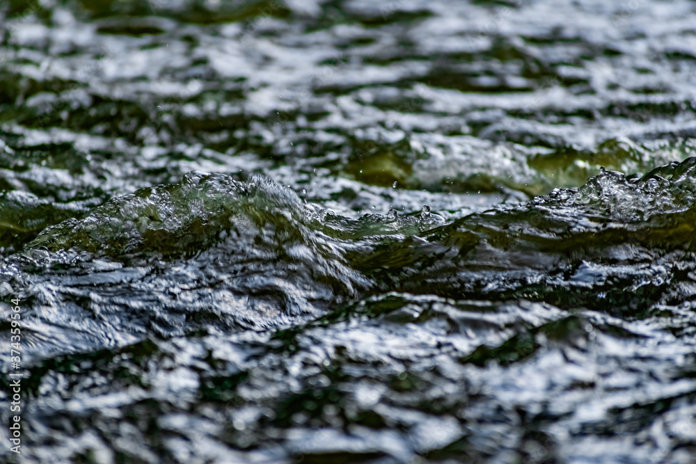 Fresh water in motion, swirling current with flying spray. Green tint on the light, transparent liquid in the river, like small waves for background and texture