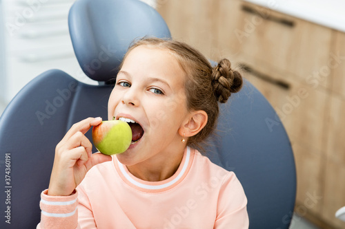 Children's teeth care. Smiling girl biting an apple, in the dentist's chair. photo