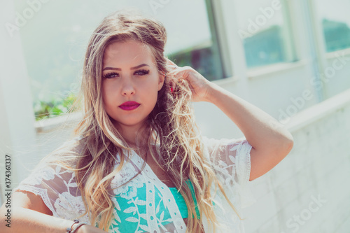 Beautiful young blonde girl with long hair blowing in the wind outdoors. Blue eyes. By the sea  light and bright colors. Day with intense sunshine.