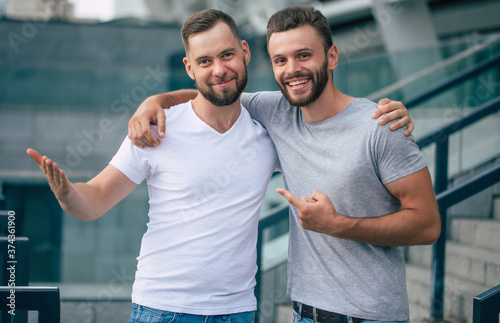 Fototapeta Two happy excited handsome bearded best friends in casual clothes are handshaking, hugging while standing outdoor