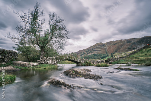 Slater Bridge, a 16th century packhorse bridge in Langdale in the Lake District shot with a slow shutter speed to show movement in the river water