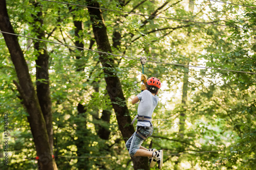 Little boy overcomes the obstacle in the rope park. Climbing in high rope course enjoying the adventure. Adventure climbing high wire forest - people on course in mountain helmet and safety equipment.