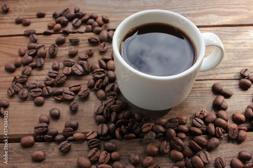 Cup of coffee with beans. Black coffee and scattered coffee beans on wooden table