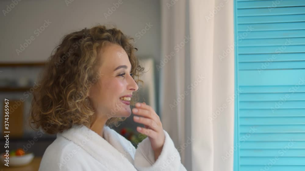 Pretty woman wearing bathrobe and standing near window while yawning after waking up. Pretty woman wearing bathrobe and standing near window while yawning after waking up.