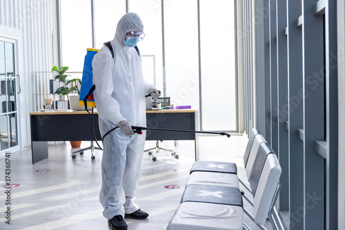 Disinfecting public place , Staff PPE uniforms suit are using an alcohol sprayer. © Pornsak