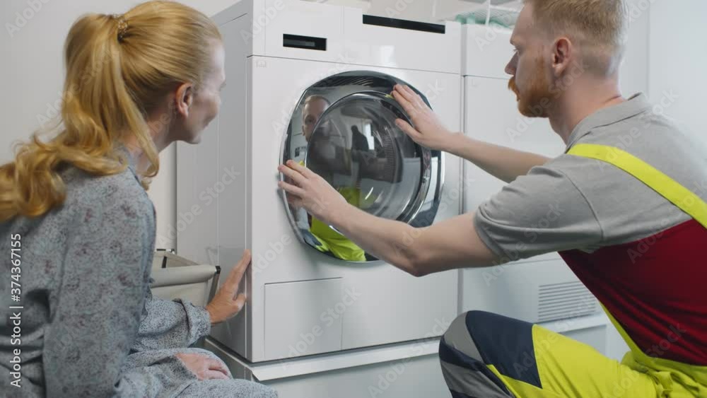 Young service man installing new washing machine and shaking hands with woman client