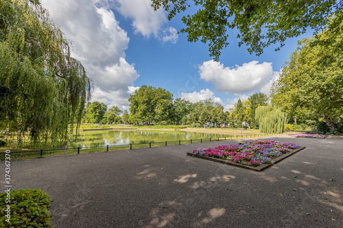 Esplanade in front of the fishing pond with planters with pink, purple, yellow and white flowers surrounded by trees in the city park, sunny day with a blue sky in Sittard, South Limburg, Netherlands photo