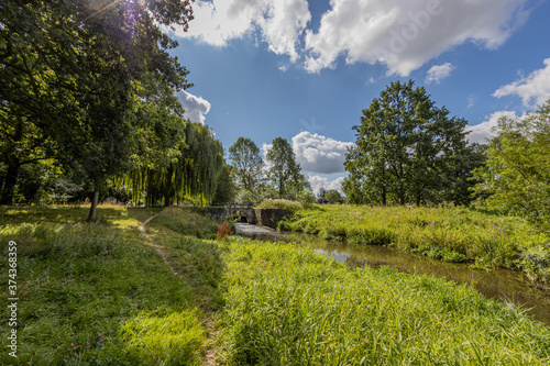Sittard city park with the Keutelbeek stream surrounded by trees and green vegetation with a small bridge over the dam and the sluice in the background, sunny summer day in South Limburg, Netherlands