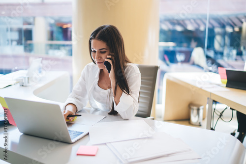 Smiling businesswoman speaking on smartphone and typing on laptop