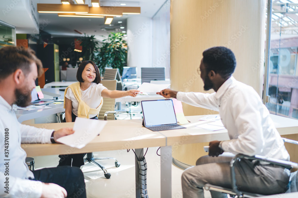 Obraz premium Smiling multiracial crew cooperating on common project in office interior share ideas and documents, positive diverse group of colleagues talking to each other collaborate in friendly atmosphere