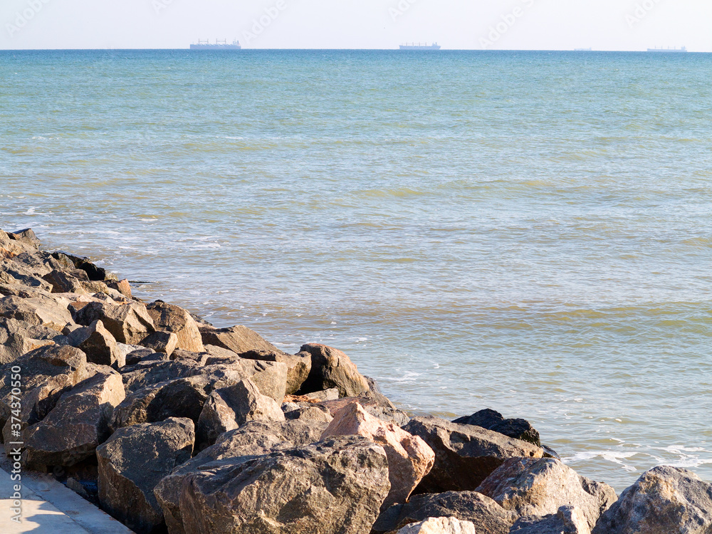 Huge stones of granite on shore of Black sea. Seascape. On horizon in haze of silhouettes of ships and buildings Huge stones of granite on shore of Black sea. Seascape. On horizon in haze of silhouettes of ships and buildings