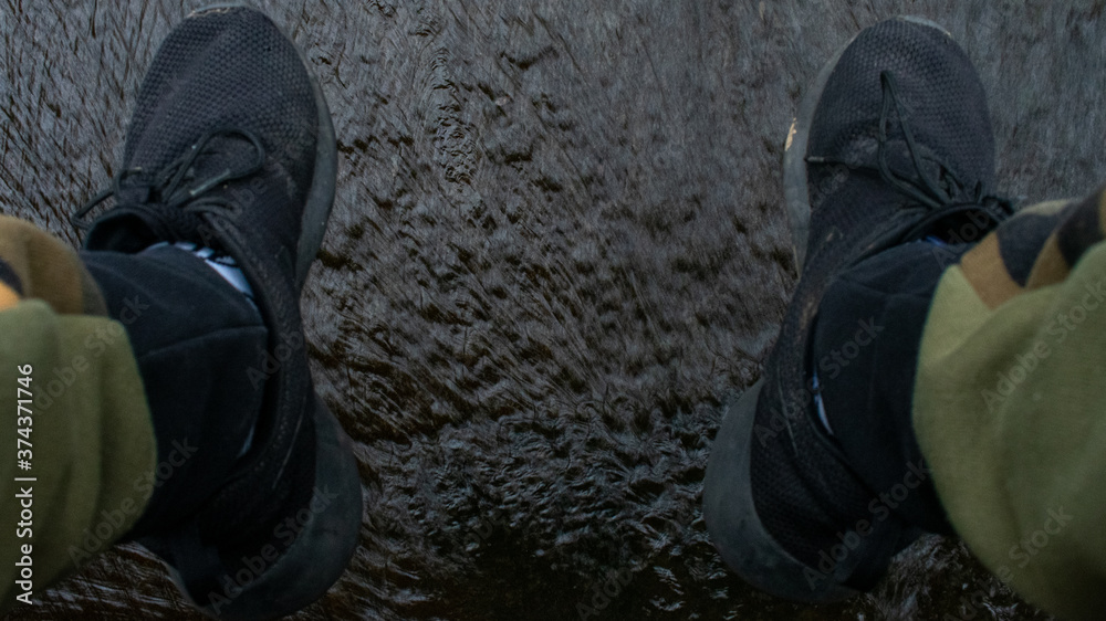 A Man's Feet in Black Shoes Dangling Over Running Water A Man's Feet in Black Shoes Dangling Over Running Water