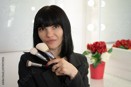 Beauty salon. attractive european woman holding professiona makeup brush, while standing over gray background. Professional visagist. Fashion makeup. Portrait close up