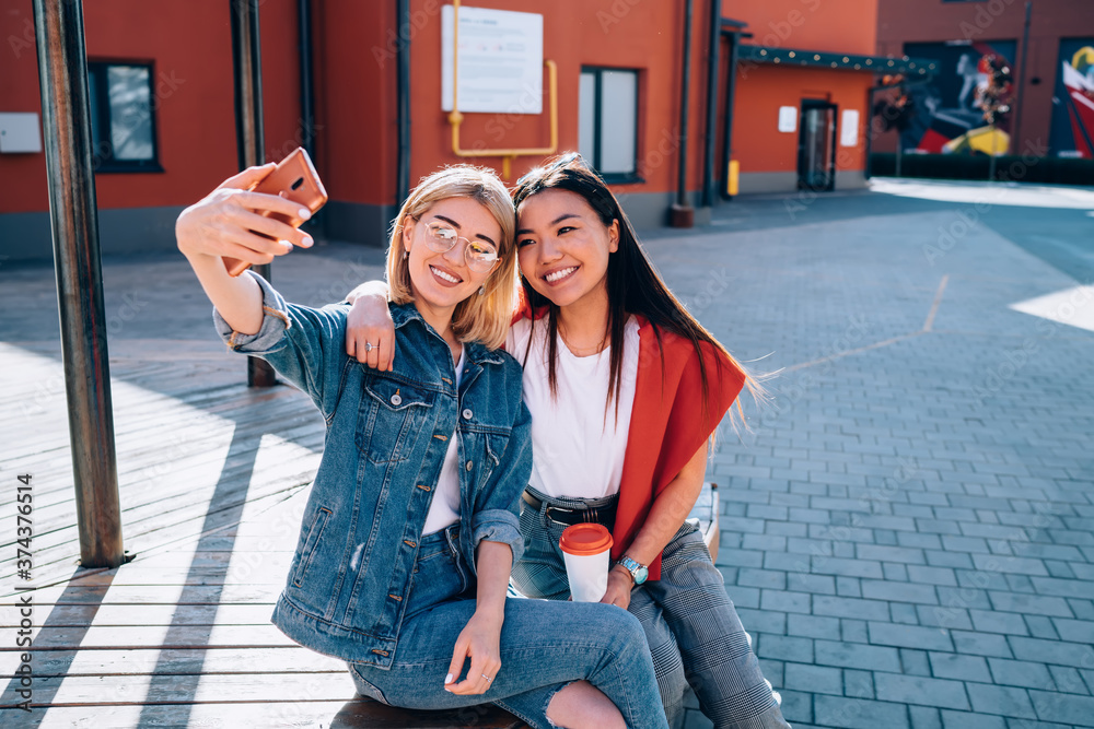 Prosperous multicultural friends spending free time together making selfie photo via smartphone for sharing to social networks, cheerful fellows taking pictures via mobile app resting outdoors Prosperous multicultural friends spending free time together making selfie photo via smartphone for sharing to social networks, cheerful fellows taking pictures via mobile app resting outdoors