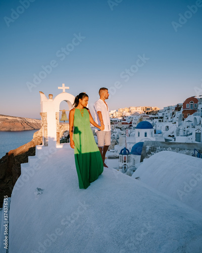 Santorini Greece, young couple on luxury vacation at the Island of Santorini watching sunrise by the blue dome church and whitewashed village of Oia Santorini Greece during sunrise during summer photo