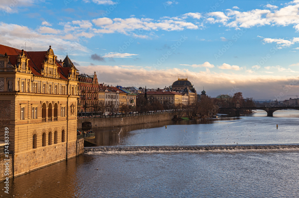 Fototapeta premium Beautiful view of Vltava river side with Bedřich Smetana Museum, National Theatre and Legion Bridge from Charles Bridge on sunny winter day with blue sky cloud, Prague, Czech Republic