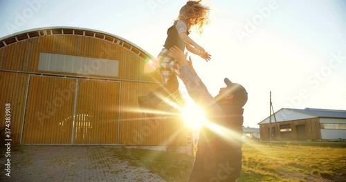 Caucasian young handsome father playing with small cute daughter and tossing up in air. Outdoor in sunlight. Farming lifestyle. Man having fun and throwing up kid at farm. Summer at countrysie. photo