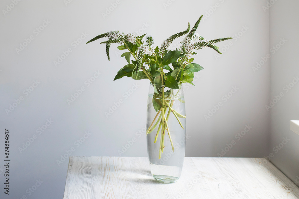 A bouquet of white veronica with white bells in a tall narrow vase on a grey table on the A bouquet of white veronica with white bells in a tall narrow vase on a grey table on the
