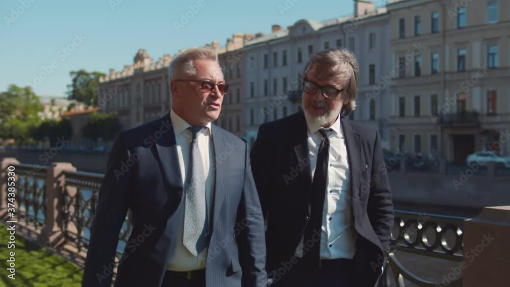 Two senior executives walking by riverside and talking during business meeting outdoors