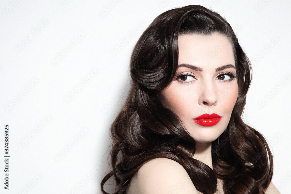 Fototapeta premium Young beautiful brunette with long curly hair and red lipstick