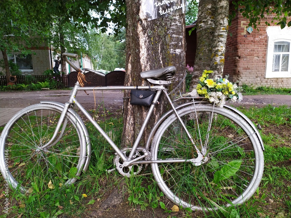 An old metal grey bicycle with a bouquet of yellow flowers by a tree