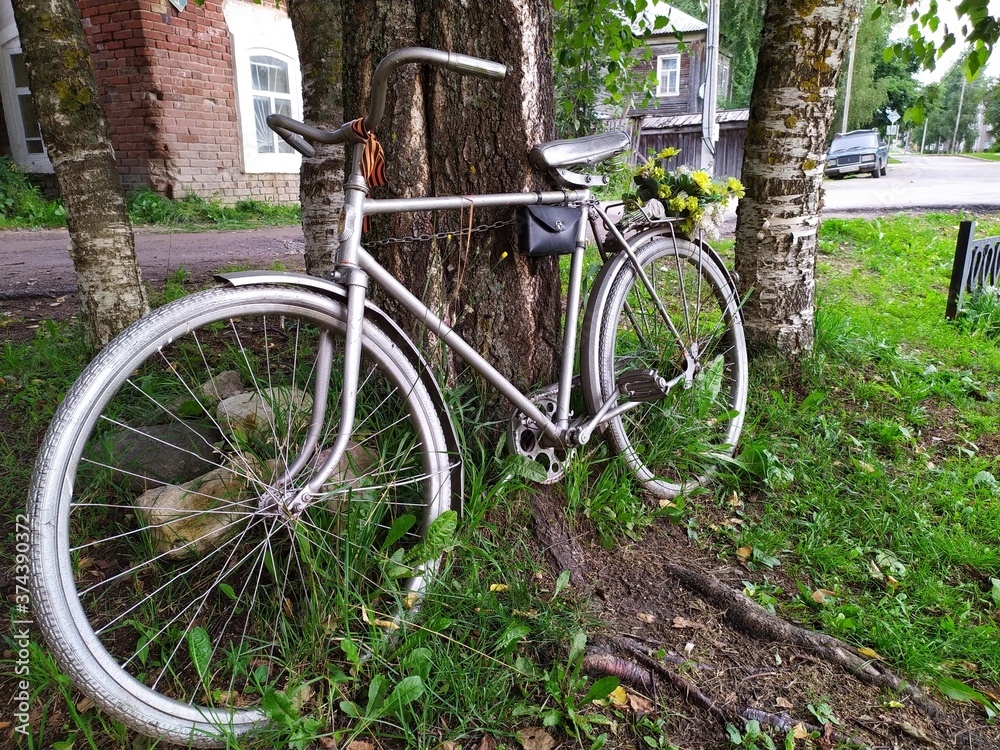 An old metal grey bicycle with a bouquet of yellow flowers by a tree