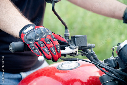 Young indian man wearing red riding gloves with protection while holding the handle bars of a motorcycle with a red tank photo