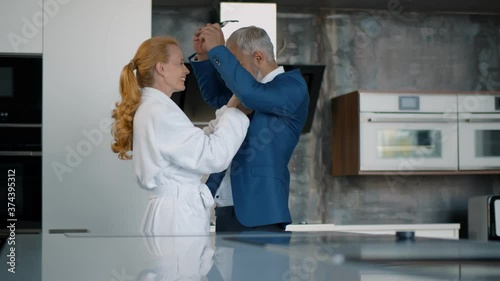 Romantic mature couple dancing in kitchen on date. Senior wife undressing husband