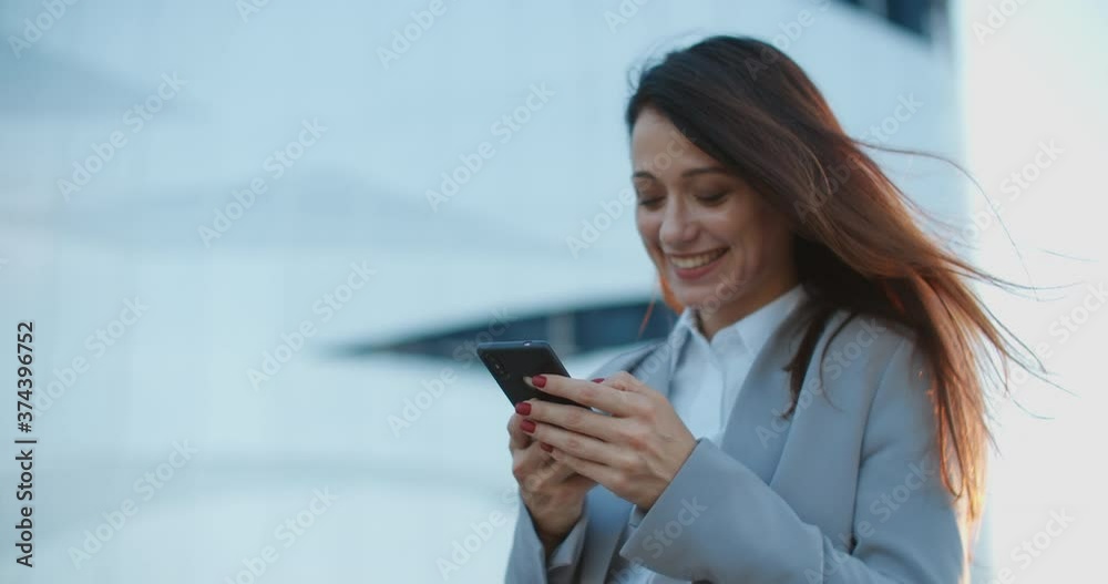 A beautiful woman in a business style stands on the street and writes a message on the phone. Female close-up portrait. High quality 4k footage