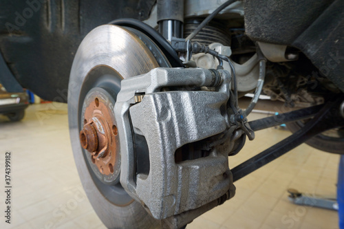 Close-up of a brake caliper mounted on a modern car. The car in the service center is lifted on a lift for repair or maintenance.