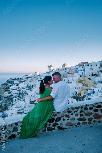 Santorini Greece, young couple on luxury vacation at the Island of Santorini watching sunrise by the blue dome church and whitewashed village of Oia Santorini Greece during sunrise during summer photo