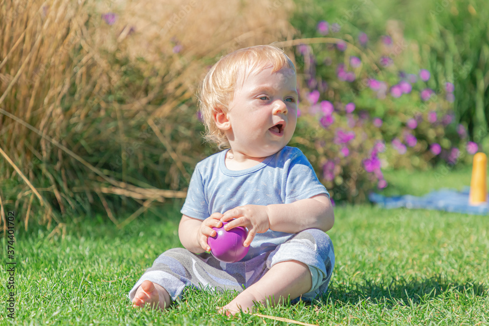 A blond boy is playing on the lawn. A happy child plays with a pyramid on the fresh green grass of a meadow. Funny kid learns the world. A blond boy is playing on the lawn. A happy child plays with a pyramid on the fresh green grass of a meadow. Funny kid learns the world.
