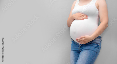 Pregnant woman holds hands on belly on a grey background. Pregnancy, maternity, preparation and expectation concept. Close-up, copy space. Beautiful tender mood photo of pregnancy.