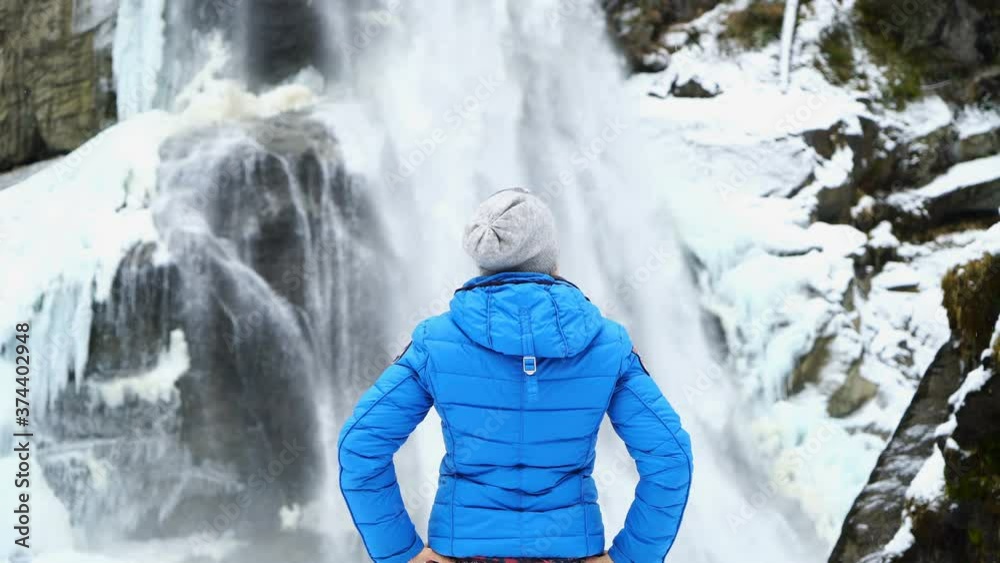 Back view of a young girl looking at waterfall during winter expedition. People travel exploration concept. 